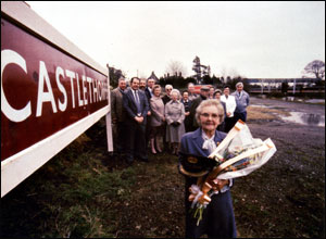Mrs Brown, the last stationmaster's wife, standing with a group of Castlethorpe villagers by the Castlethorpe Station sign.